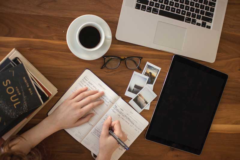 person taking notes at his desk with a coffee